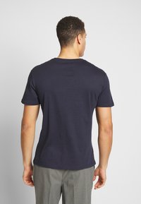 Camiseta de manga corta de color azul marino con cuello redondeado. Tejido suave y liso sin patrones visibles ni elementos metálicos. Diseño ajustado.