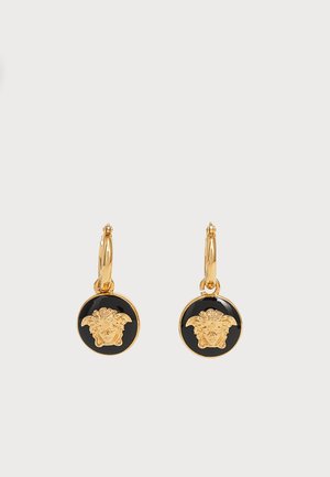 Boucles d’oreilles créoles en or avec des pendentifs circulaires noirs ornés d’un motif en relief représentant une tête de Méduse dorée sur chaque pendentif.
