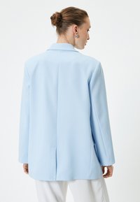 Blazer su misura di colore blu chiaro con rever a punta, apertura posteriore singola e maniche lunghe. Tessuto morbido e vestibilità rilassata.