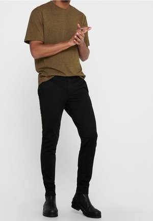 Olivgrön texturerad t-shirt i kombination med svarta slim-fit byxor och svarta ankelstövlar, med en minimalistisk design utan synliga mönster.