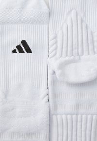 Bijele sportske čarape s rebrastom teksturom; sadrže crni Adidas logo sa strane. Dizajnirane za udobnost i prilagodljivost tijekom sportskih aktivnosti.