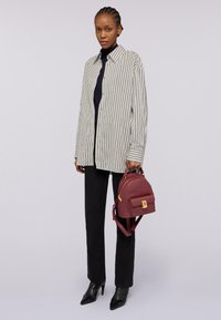 Proužkovaná oversized košile v bílé barvě s černými pruhy, černý rolák, černé kalhoty a bordó taška se zlatými kovovými detaily. Černé špičaté lodičky.