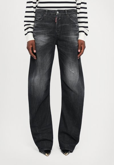 Jean en denim large, de couleur gris foncé avec des détails délavés, des poches et une légère déchirure. Associé à un pull rayé noir et blanc.