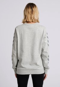 Sweat-shirt gris à manches longues, avec poignets et ourlet côtelés. Présente des rayures diagonales gris foncé sur les manches. Tissu doux et texturé.