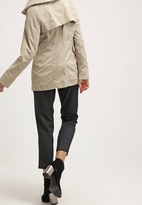 Chaqueta ligera beige con un gran cuello, cierre de botones y una textura sutil, combinada con pantalones gris ajustados y botines negros con tacón.