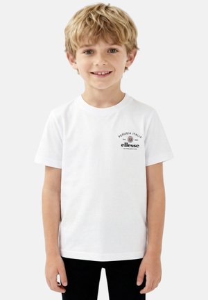 Garçon blond souriant portant un t-shirt blanc ellesse avec le logo "Perugia Italia" sur la poitrine, debout devant un fond clair uni.