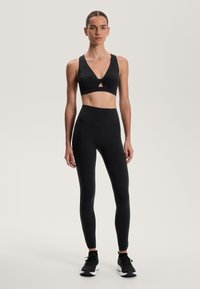 Set sportiv negru, compus dintr-un bralet cu detalii în formă de lacăt și colanți cu talie înaltă asortați. Material neted, design ajustat, accente minime.