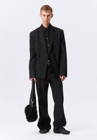 Svartstripete dress med en skreddersydd passform, kombinert med en svart skjorte. Holder en rund, fuzzy svart veske med en stropp.