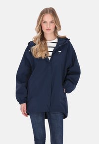 Sötétkék vízálló kabát kapucnival, laza szabással, elasztikus mandzsettákkal és elülső zsebekkel. A mellkason egy kis fehér esernyő logó található.