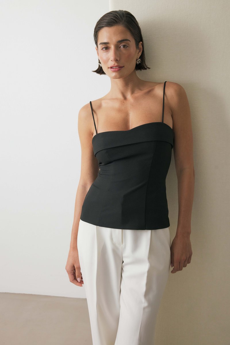 Juodas prigludęs kamšalas su plonomis petnešomis, turintis struktūrizuotą liemenį ir lygų audinį. Suderintas su baltais, laisvai krentančiais kelniais.