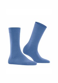 Une paire de chaussettes unies bleu marine, l'une debout et l'autre inclinée à droite sur un fond blanc.