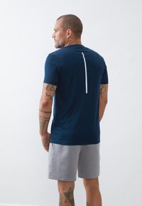 Camiseta atlética azul-marinho com mangas curtas, apresentando uma faixa branca vertical nas costas. Emparelhada com calções cinzentos, mostrando um tecido texturizado.