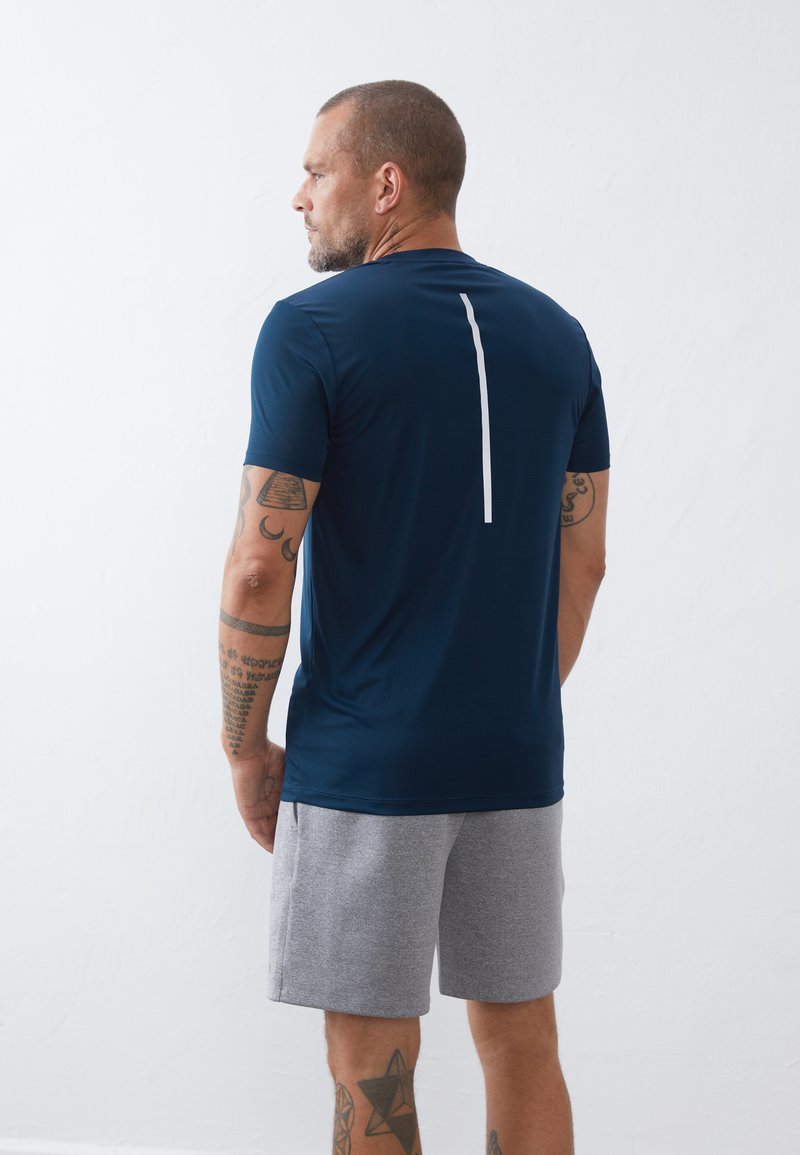 Camiseta deportiva de color navy con mangas cortas, que presenta una franja blanca vertical en la parte posterior. Combinada con pantalones cortos gris, mostrando una tela texturizada.