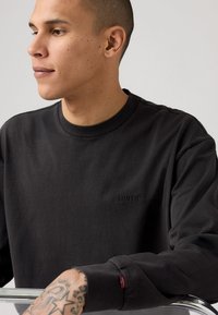 Schwarzer Rundhalsausschnitt-Sweatshirt aus Baumwolle. Verfügt über ein dezentes schwarzes Levi's-Logo und ein kleines rotes Etikett am Ärmel. Glatte Textur.