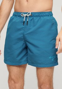 Blauwe zwemshorts met een geometrisch patroon, elastische tailleband, koordsluiting en zijzakken.