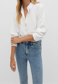White button-up shirt with a collar, rolled sleeves, paired with high-waisted blue denim jeans with a faded wash and minimal distressing.