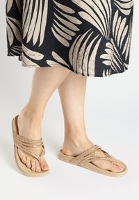 Beige Flip-Flops verfügen über einen strukturierten Riemen, der mit Glitzer verziert ist, und haben eine glatte Sohle. Das Design umfasst eine V-Form und eine offene Zehenpartie.
