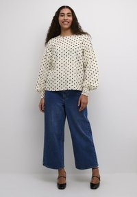 Lichte crèmekleurige blouse met zwarte stippen, met smock-mouwen, gecombineerd met donkerblauwe wijde jeans en zwarte hakken. Glad textuur van de stof.