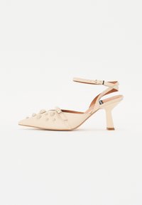 Béžová slingback obuv s ostrou špičkou a štruktúrovaným zvrškom, ktorý je zdobený okrúhlymi hrotmi, nastaviteľným remienkom okolo členka a širokým, zúženým podpätkom.