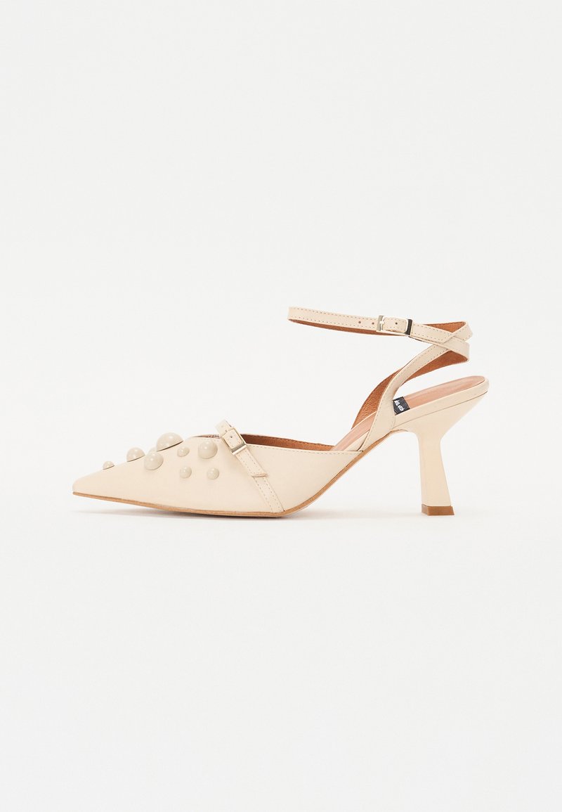 Béžová slingback obuv s ostrou špičkou a štruktúrovaným zvrškom, ktorý je zdobený okrúhlymi hrotmi, nastaviteľným remienkom okolo členka a širokým, zúženým podpätkom.