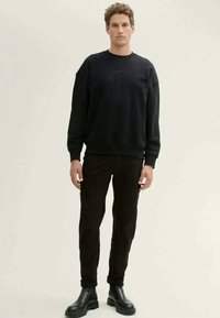 Black crew-neck sweatshirt in a relaxed fit, paired with slim black pants and shiny black ankle boots. Smooth texture, minimal design.
