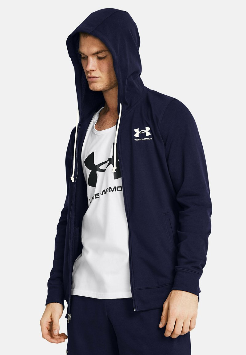 Felpa con zip navy e coulisse, con logo Under Armour; tessuto soffice, vestibilità regolare, abbinata a una canotta bianca con logo nero.
