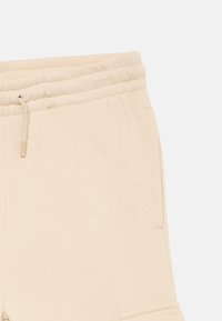 Beige elastic waistband shorts with a drawstring and side pocket, made from soft, textured fabric.