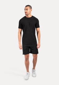 Camiseta negra de manga corta combinada con pantalones cortos negros, confeccionada en un tejido suave y elástico, usada con zapatillas blancas. Diseño geométrico limpio.