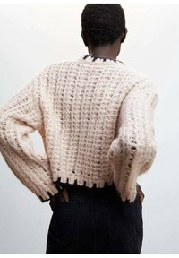 Maglione lavorato a maglia rosa chiaro con trama a rete aperta e rifinitura nera all'orlo. La modella è di spalle e indossa jeans scuri.