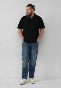 Zwarte polo met korte mouwen, gecombineerd met blauwe jeans en witte sneakers. De polo heeft een klein logo op de linkerborst.