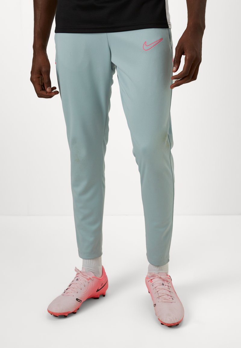Lyseblå træningsbukser med pink Nike-logo, taperet fit, elastisk talje og ribbede ankler. Båret med pink fodboldstøvler.
