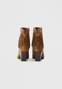Botine din suede maron cu un design franjurat și toc pătrat. Dispun de un vârf rotunjit și deschideri laterale pentru o purtare ușoară.