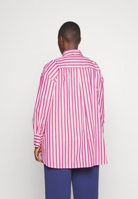 Camisa de manga larga con rayas verticales rosas y blancas, con cuello tipo camisa, detalles de botones y un corte holgado.