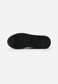 Suela de zapatilla negra con ranuras y relieves horizontales, que presenta una punta redondeada y un emblema circular de marca en el área del talón.