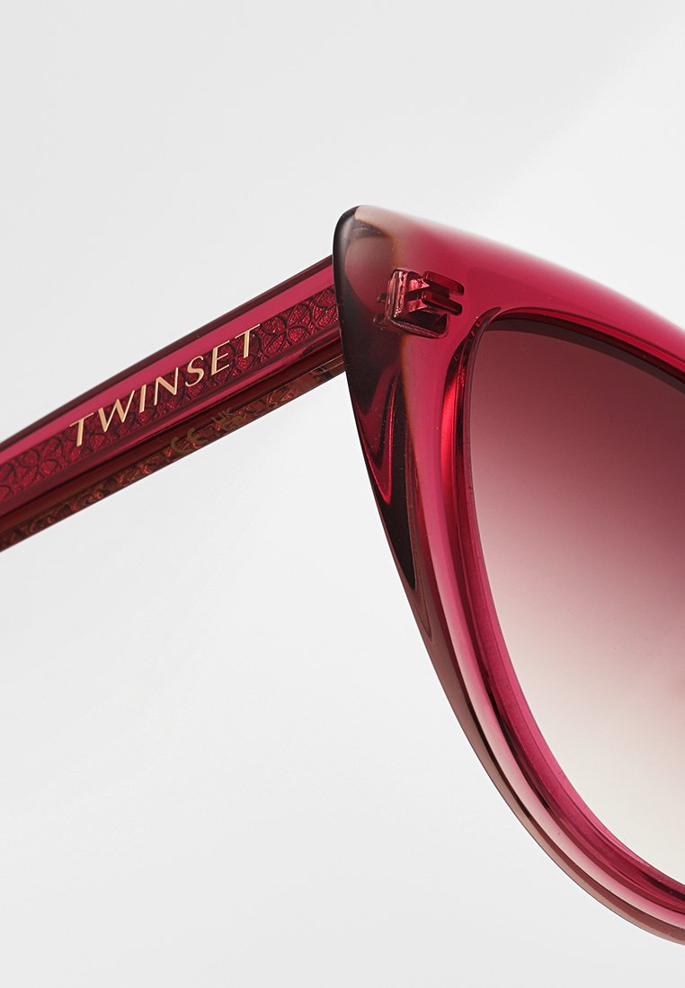 Rote Cat-Eye-Sonnenbrille mit verlaufenden Gläsern und glänzender Oberfläche. Rahmen verziert mit einem gemusterten Bügel und goldfarbenem "TWINSET"-Logo.
