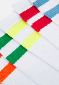 Calzini bianchi con texture a costine, caratterizzati da righe orizzontali in rosso, blu, giallo, verde e arancione nella parte superiore.