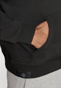 Μαύρη φούτερ με ριγωτούς μανσέτες και τελείωμα, που διαθέτει μπροστινή τσέπη και ετικέτα λογότυπου στο κάτω μέρος. Μαλακή �υφή και χαλαρός σχεδιασμός.