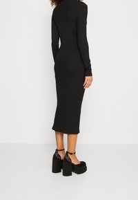 Schwarzes, geripptes Midikleid mit langen Ärmeln und enganliegendem Schnitt, kombiniert mit klobigen schwarzen Plateauschuhen mit Knöchelriemen.