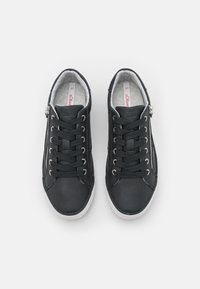 Ett par svarta låga sneakers med vita sulor, svarta snörningar och sidodragkedjor, sedd ovanifrån mot en vit bakgrund.