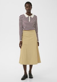 Haut à manches longues rayé avec un col blanc, associé à une jupe évasée beige. Le mannequin porte des mocassins noirs. Les textures lisses dominent.