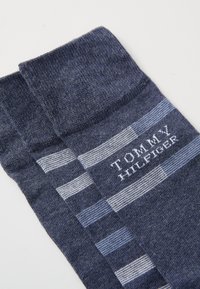 Marineblaue Socken mit blau-weißen Streifenmustern, die das "TOMMY HILFIGER"-Logo in Weiß aufweisen. Weicher Strickstoff, standardmäßige Crew-Länge.