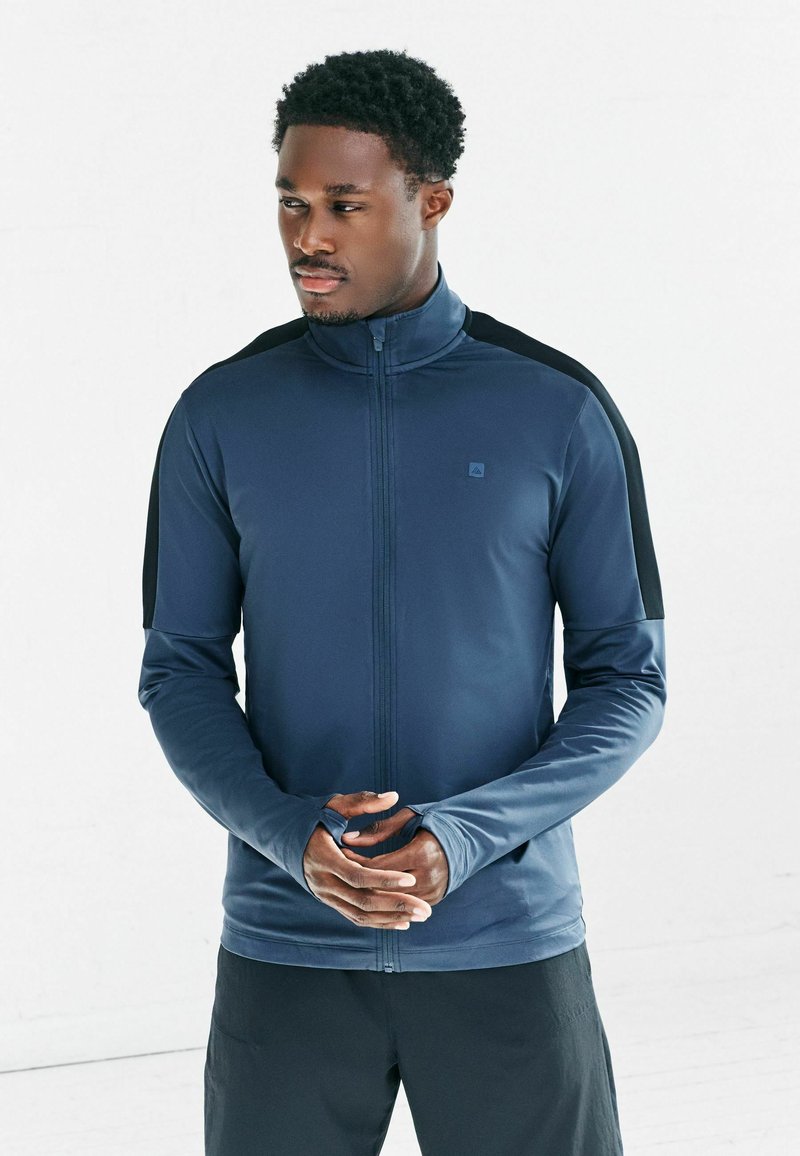 Granatowa sportowa kurtka na zamek błyskawiczny z czarnymi akcentami na ramionach, długimi rękawami z otworami na kciuki i dopasowanym krojem.