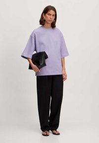 Lavender oversized T-shirt with short sleeves, paired with wide black trousers. Black pouch clutch; model wearing flat black sandals.