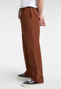 Pantalons légers marron avec une taille à cordon, poches latérales et un design à jambe droite, associés à des baskets noires et blanches.