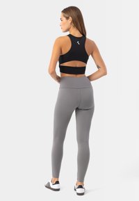 Černý sportovní crop top s výřezem na zádech, doplněný o šedé legíny s vysokým pasem. Modelka má na sobě černobílé tenisky.