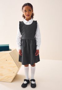 Tumehall kleit volangidega rihmadega, valge kraeuga särk ja põlvekõrgused valged sokid. Mustad kingad, millele on lisatud paelad, lõpetavad riietuse.