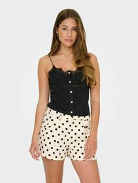 Svart cami med spetsdetaljer och knappar, tillsammans med krämfärgade shorts i svart prickmönster. Båda plaggen har en klassisk och avslappnad design.