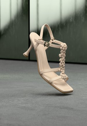 Μπεζ γυναικεία πέδιλα με ψηλό τακούνι και τετράγωνη μύτη, με λεπτά λουράκια στον αστράγαλο και διακοσμητικό λουλούδι στο κέντρο. Ομαλή υφή.