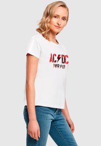T-shirt bianco in cotone con stampa grafica rossa e nera "AC/DC PWR UP". Maniche corte, vestibilità rilassata, abbinato a jeans blu.