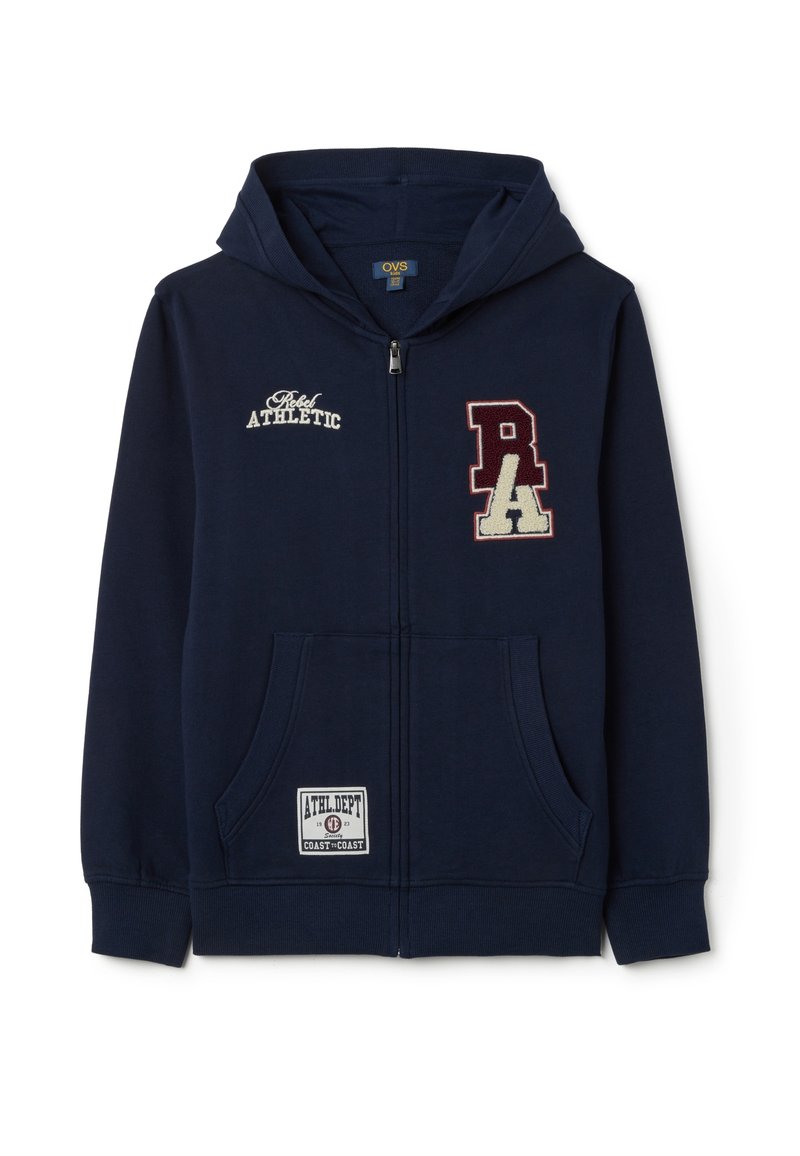 La sudadera azul marino presenta un cierre frontal con cremallera, dos bolsillos laterales y parches bordados con texto. Tejido suave con puños y dobladillo acanalados.